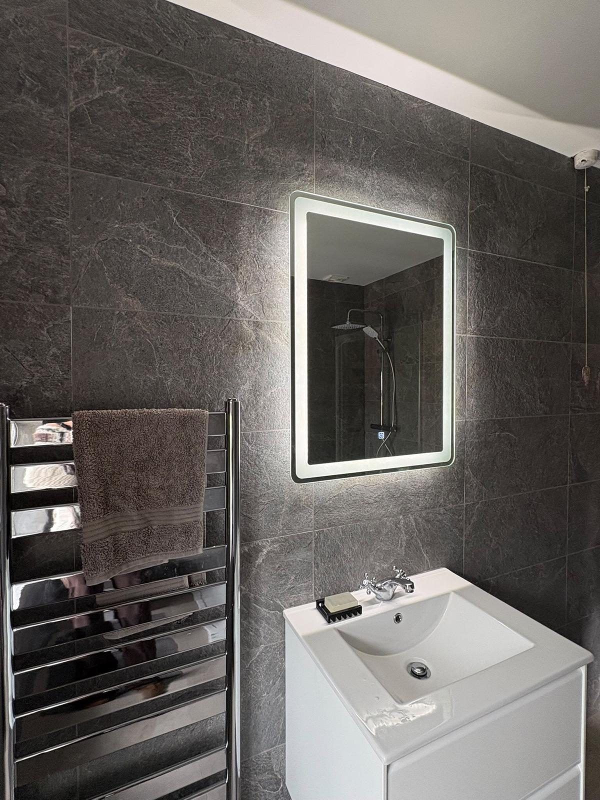 Backlit LED mirror above a vanity basin beside a chrome towel rail