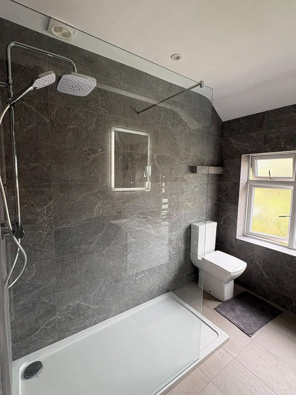 Walk-in shower with a rainfall head and a fixed glass screen in grey slate-effect tile