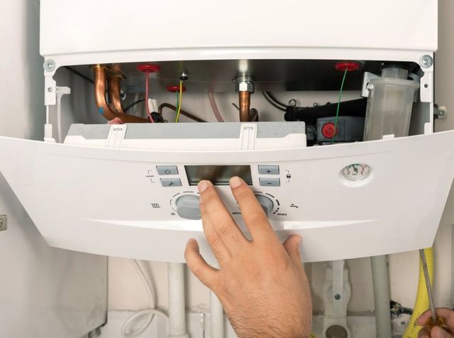 Hand on the control panel of a wall-mounted gas boiler with its cover off