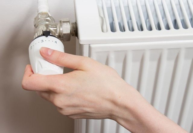 Hand adjusting a thermostatic valve on a white radiator