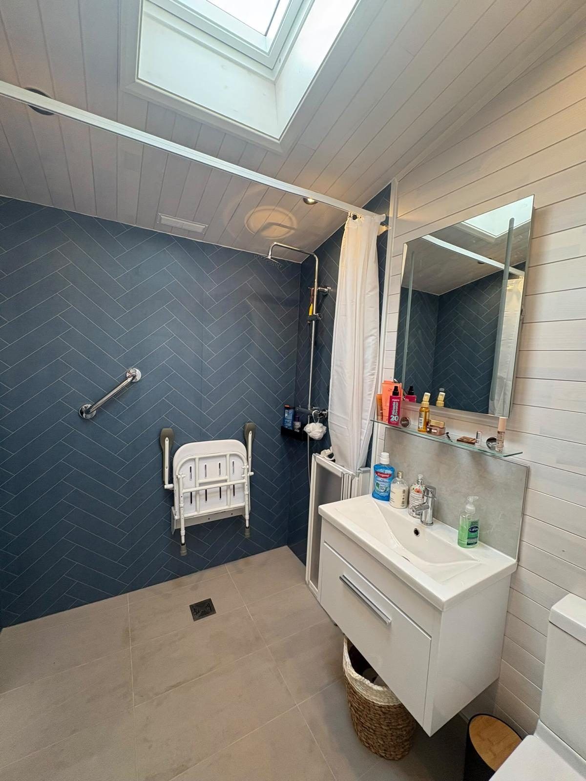 Wet room with blue herringbone wall boards, a fold-down seat and a white vanity unit under a roof window