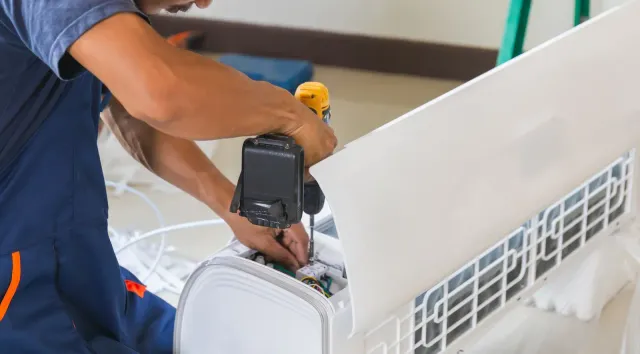 A man is fixing an air conditioner with a screwdriver.