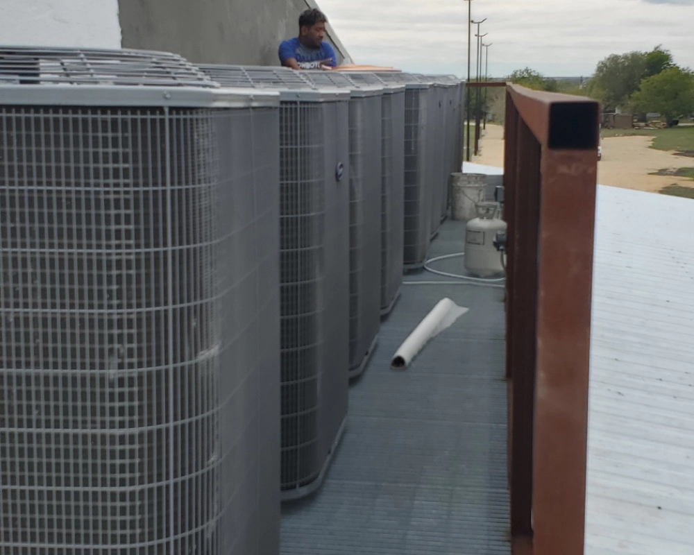 A man standing on top of a roof next to a row of air conditioners