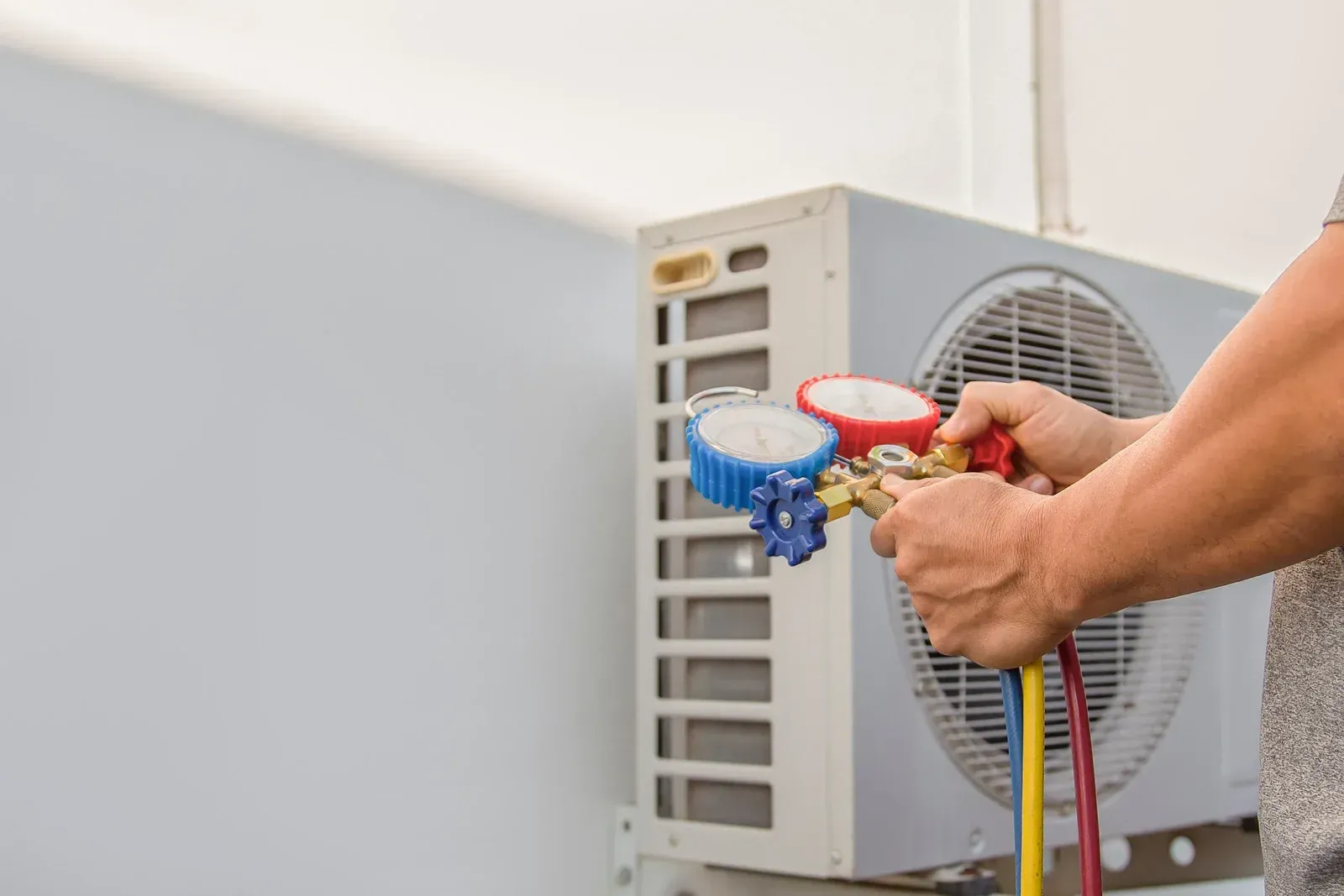 Person using gauges on an air conditioning unit outside, measuring pressure.