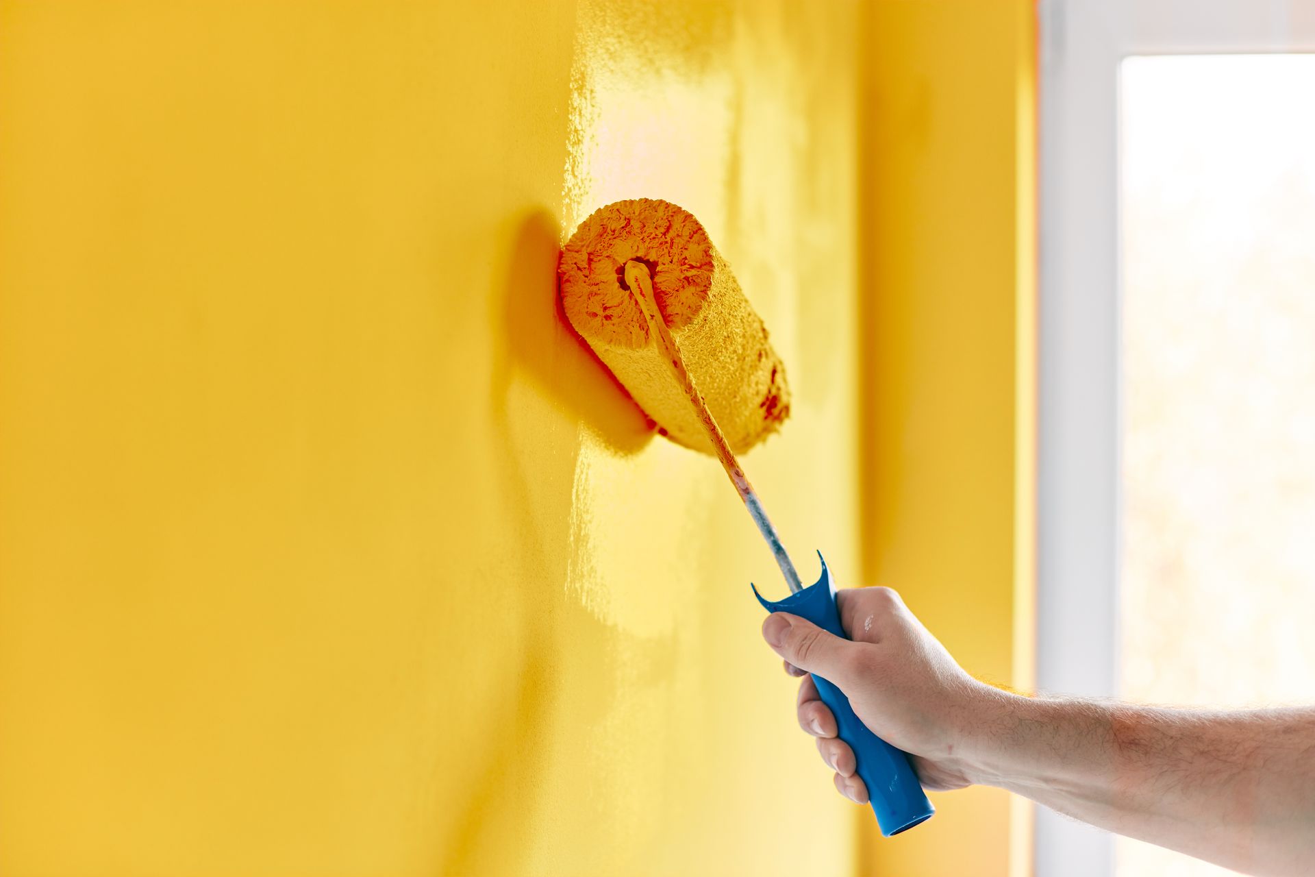 Hand using a paint roller to apply yellow paint on a wall