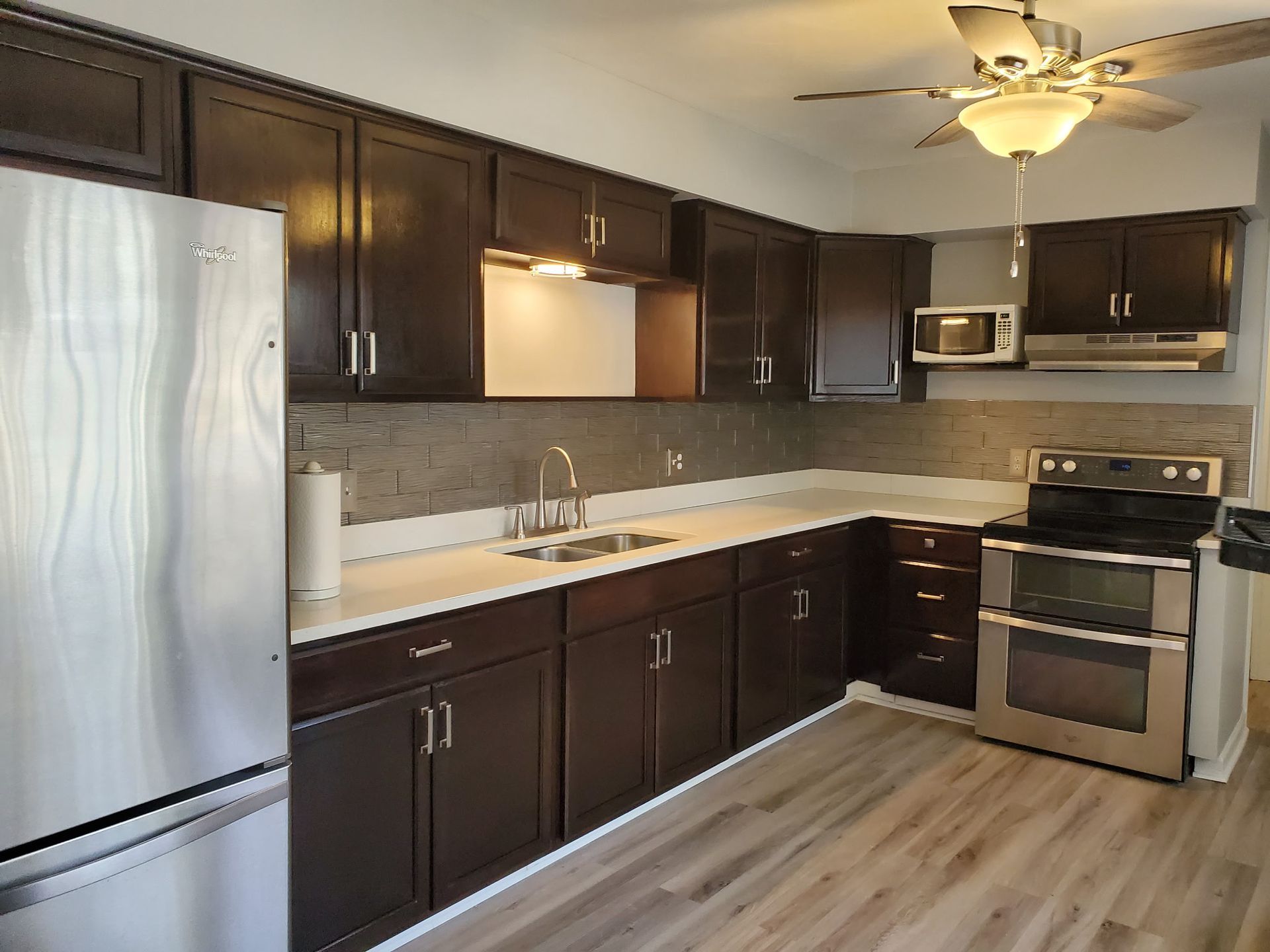 Dark wood kitchen cabinets, stainless steel appliances, white countertops, and wood-look flooring.