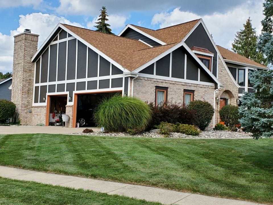 House with brown roof, gray siding, brick, and two-car garage, on a green lawn.