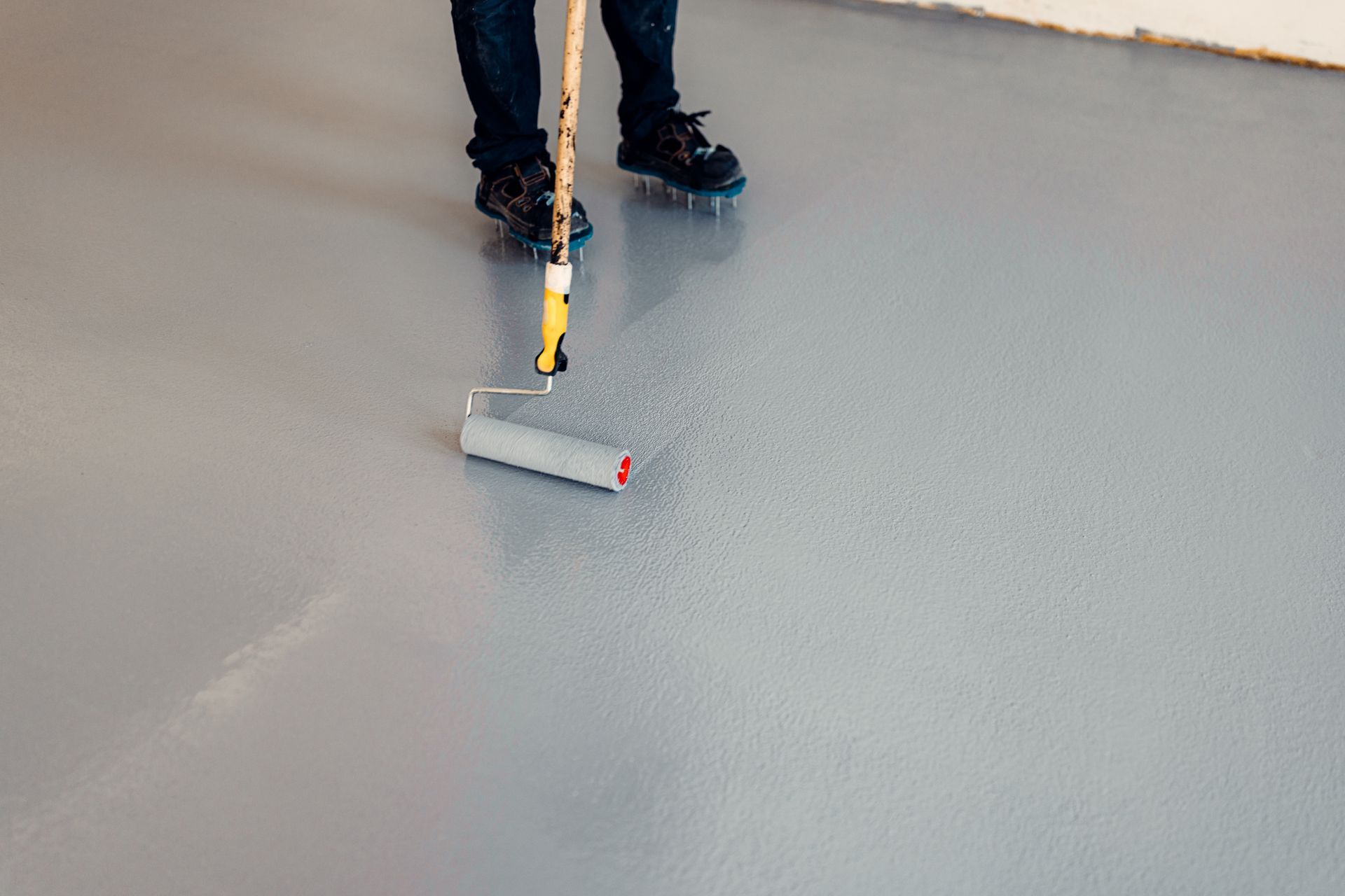 Person applying gray epoxy coating to a floor with a roller.