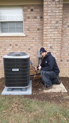 A man is kneeling down next to an air conditioner in front of a brick building.