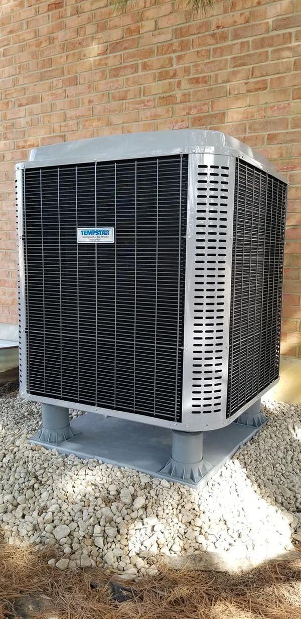 A large air conditioner is sitting outside of a brick building.