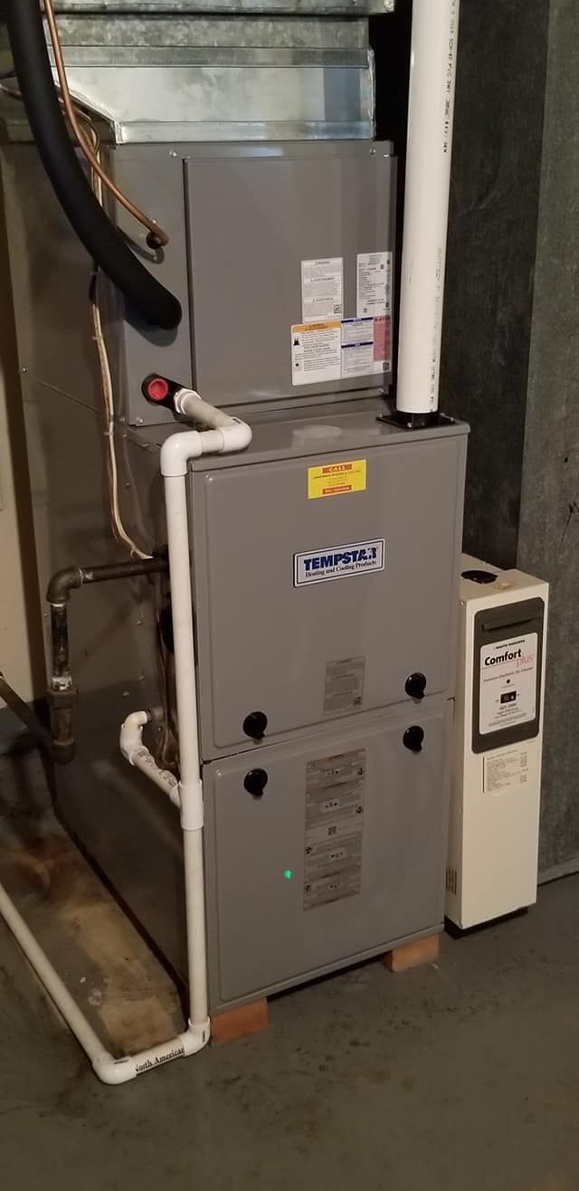 A gray furnace is sitting in a basement next to a white box.