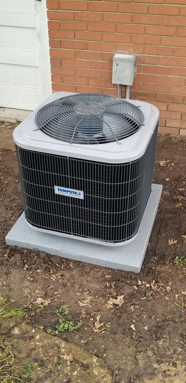 An air conditioner is sitting in the dirt in front of a brick building.