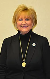 A woman in a black suit and gold necklace is smiling for the camera.