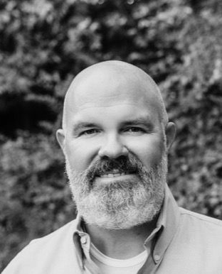 A bald man wearing a plaid shirt and khaki pants