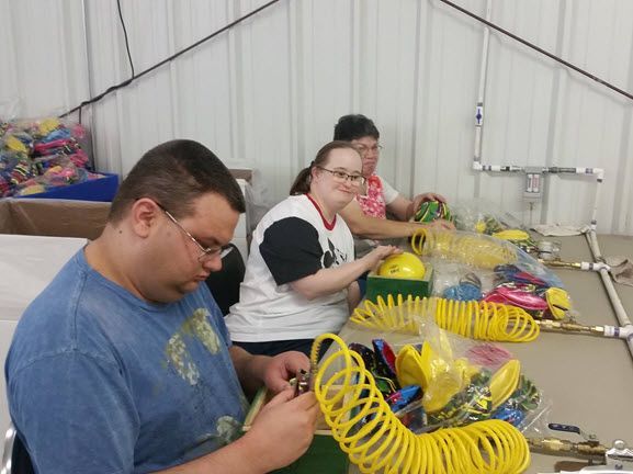 A group of people are sitting at a table working on balloons