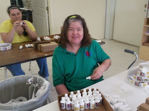 A woman in a green polo shirt is sitting at a table with bottles on it