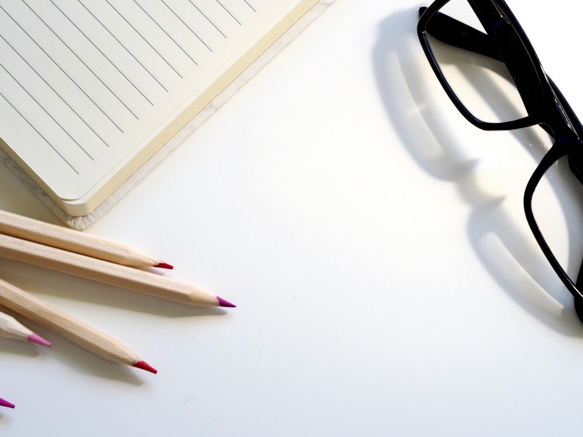 A pair of glasses sits next to a notebook and pencils
