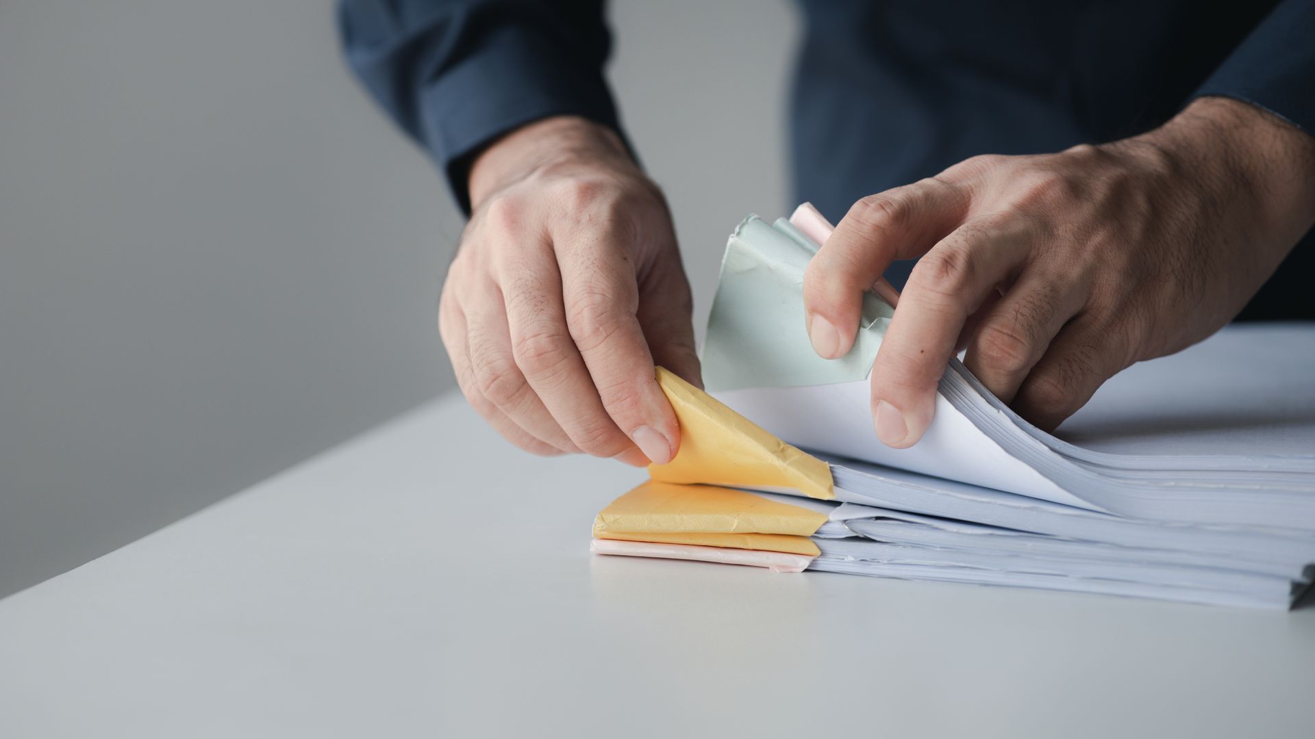 A person is putting sticky notes on a stack of papers.