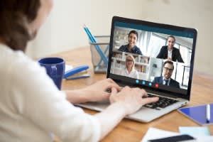Person on video call using a laptop, view of other participants on screen, at a desk.