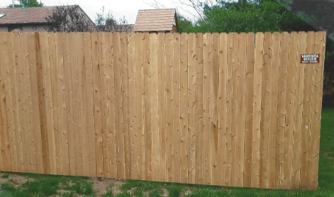 A close up of a wooden fence with a bush in the background.