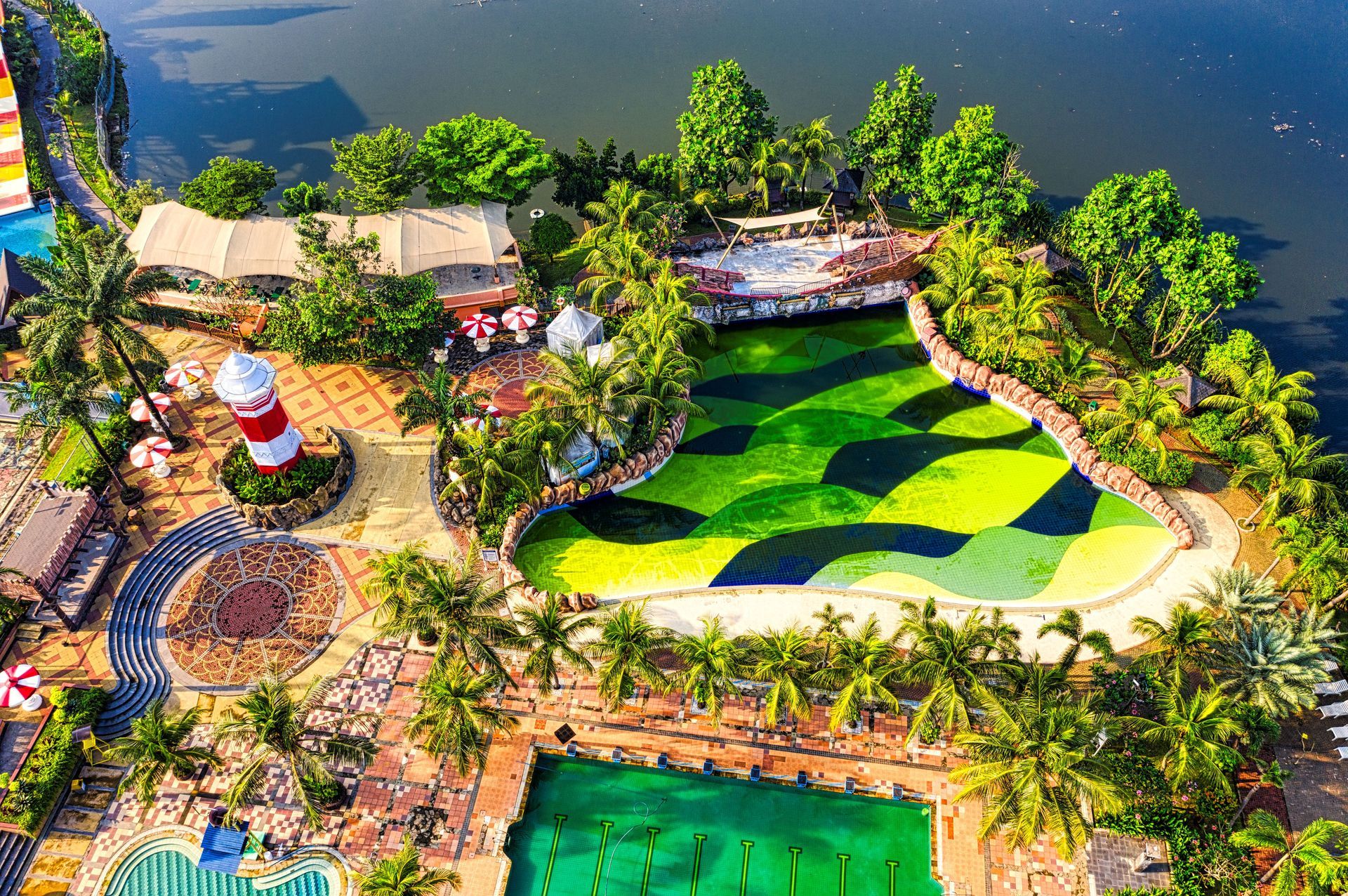 Aerial view of a colorful lakeside resort with gardens, buildings, and a green patterned lawn