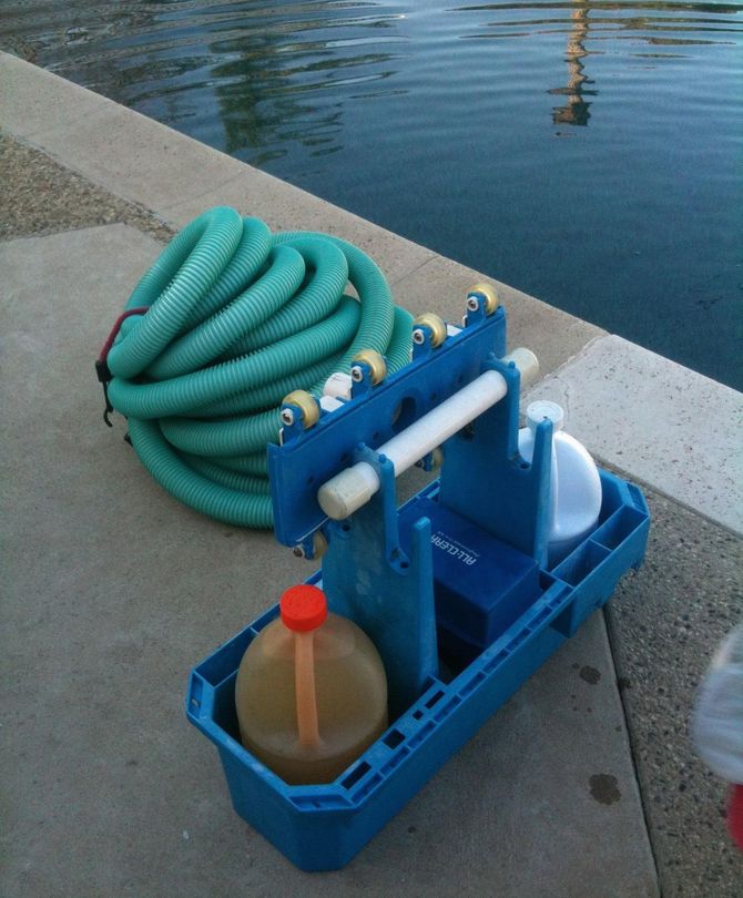 Blue dockside cleanup setup with coiled green hose and plastic containers beside the water