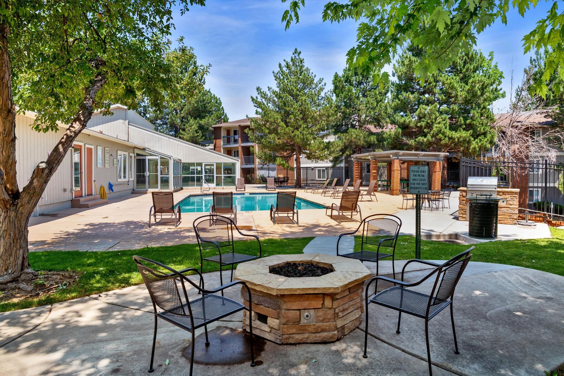 Outdoor area with fire pit, pool, seating, and trees on a sunny day.