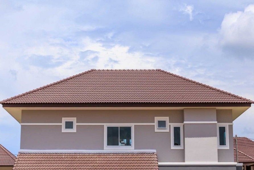 Two-story house with beige walls and a reddish-brown tiled roof under a blue sky