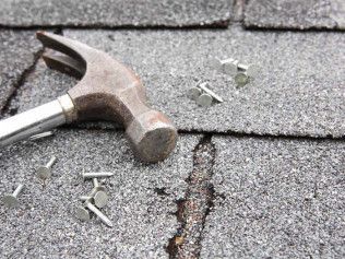 Hammer on asphalt shingles beside a damaged roof seam with scattered nails