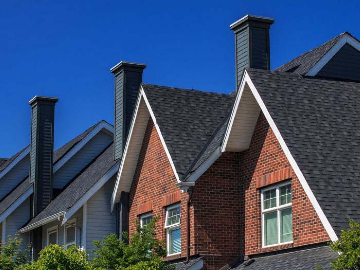 Row of brick and gray suburban houses with steep gabled roofs and chimneys under blue sky