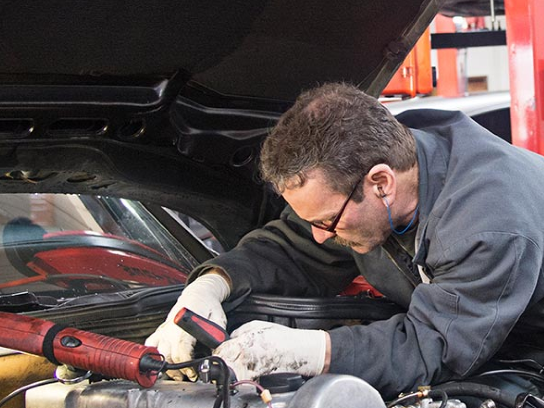 A mechanic working on a car engine under the hood in a repair shop