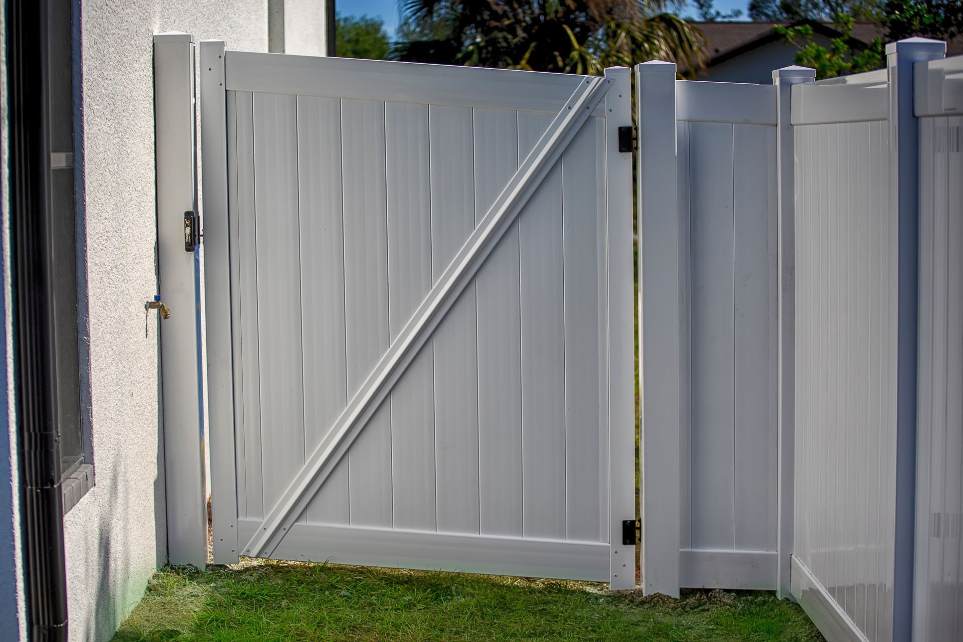 White vinyl gate in a yard, diagonal brace for support, attached to white fence and house.
