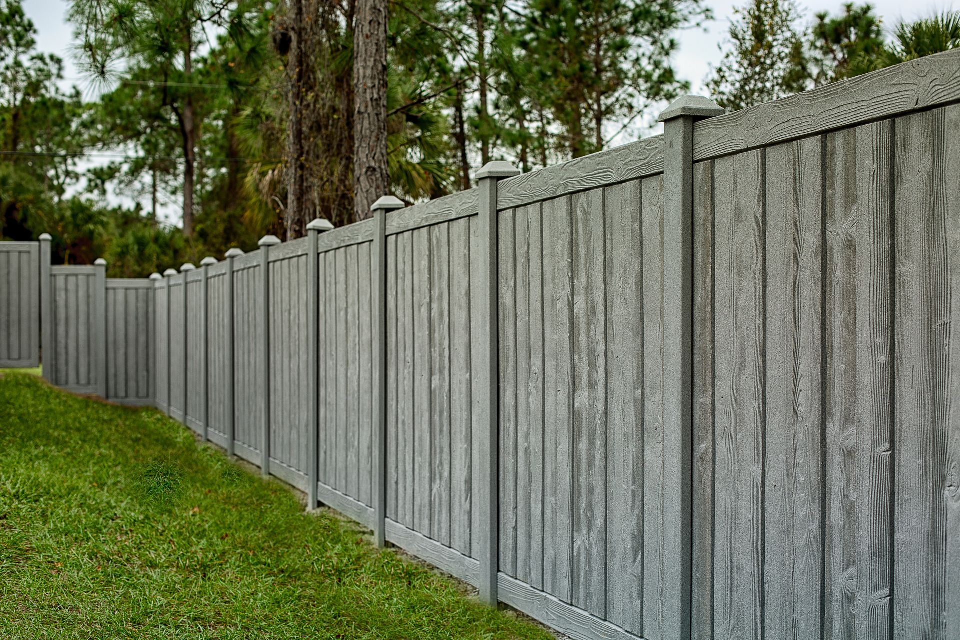 Gray composite privacy fence in a grassy yard, trees in the background. Gray composite privacy fence in a grassy yard, trees in the background.
