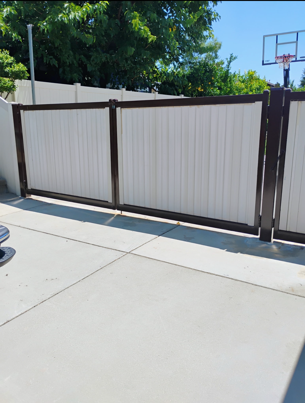 White and brown fence with basketball hoop in a yard on a sunny day. White and brown fence with basketball hoop in a yard on a sunny day.