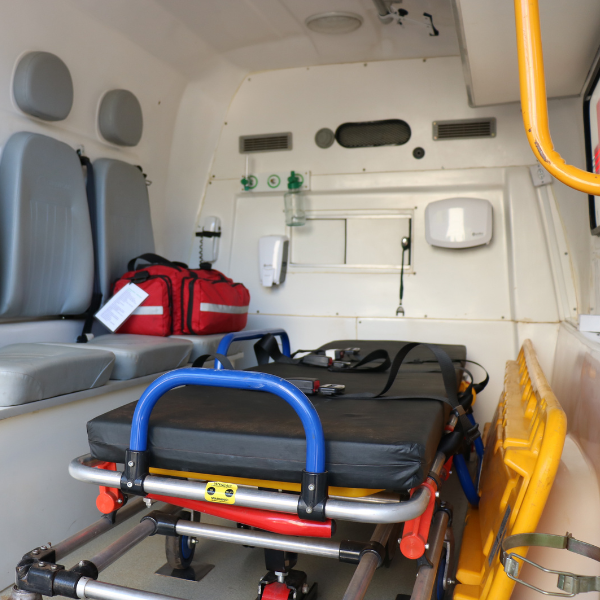 Dentro de uma ambulância, uma maca com grades azuis e equipamentos médicos prontos para o transporte de pacientes.