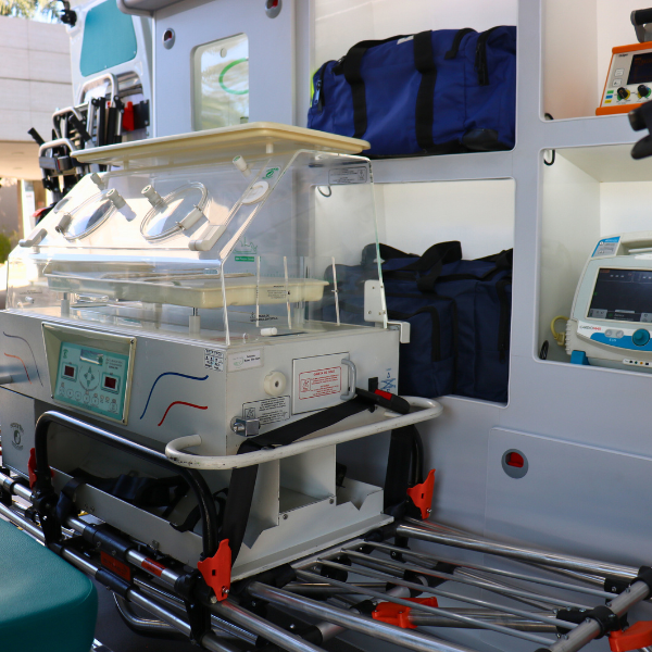 Maca de transporte hospitalar com incubadora infantil e equipamentos médicos no interior de uma ambulância.