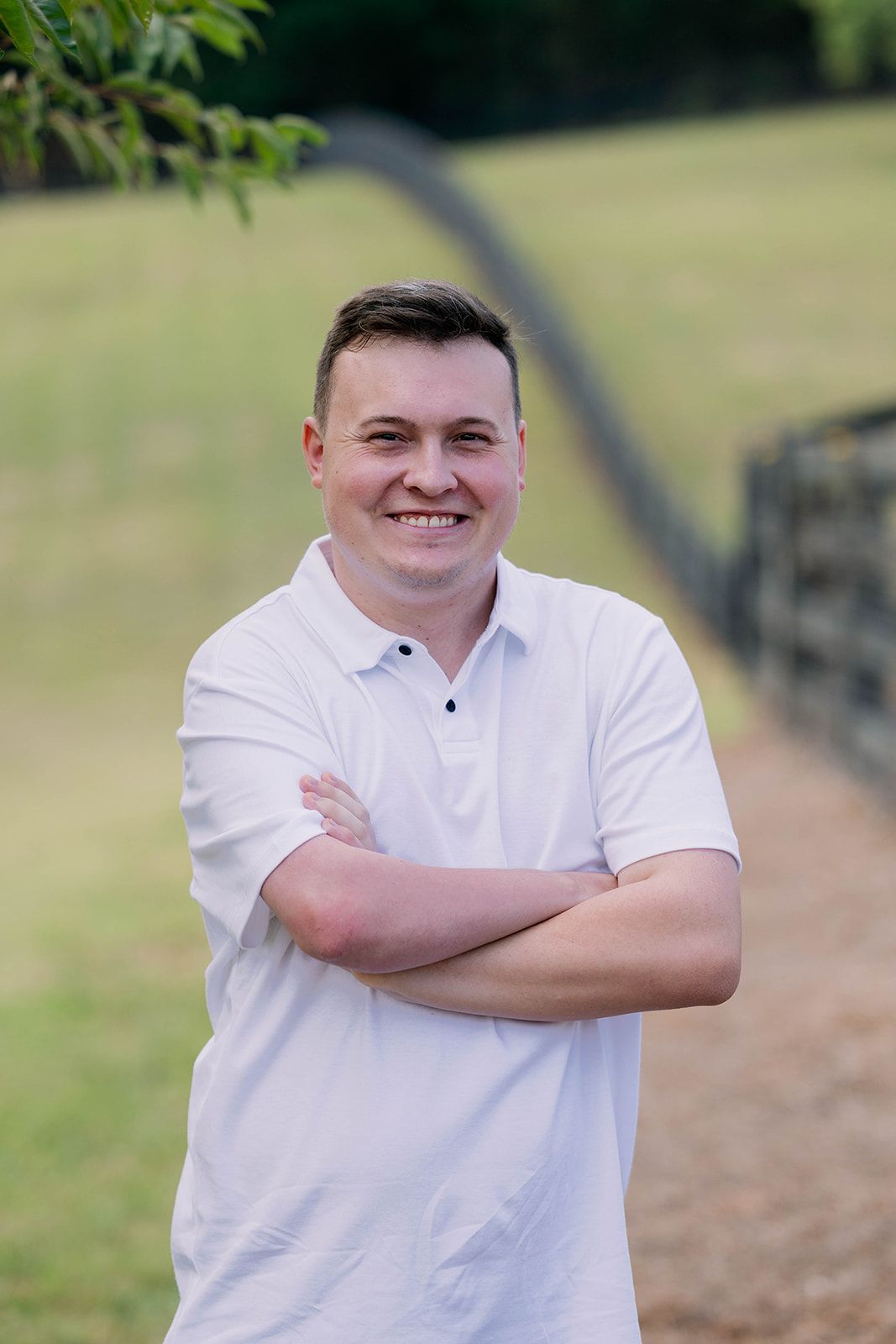 Smiling person in a white shirt with arms crossed on a blurred outdoor path