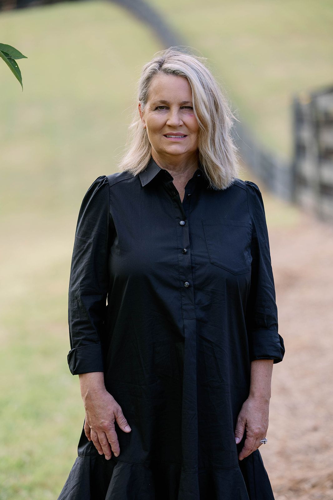Woman in a black dress standing outdoors with a blurred grassy background
