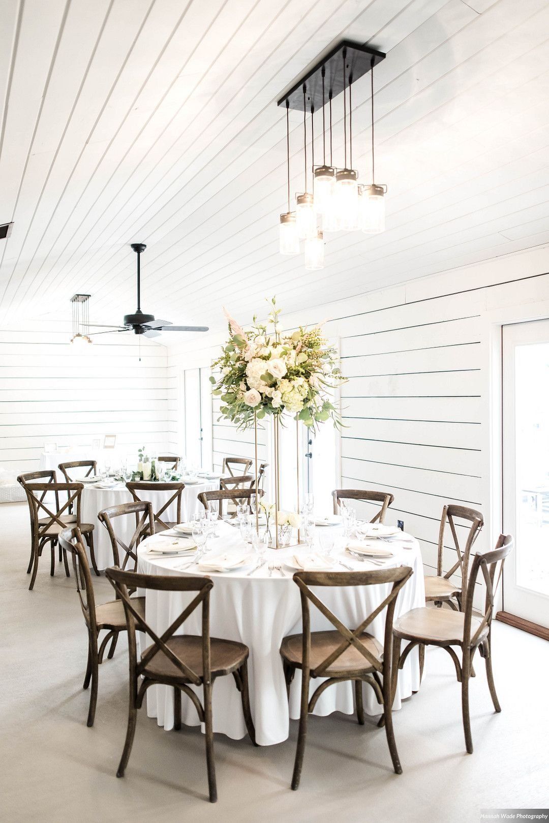 Bright white dining room with round tables, wooden chairs, and floral centerpieces