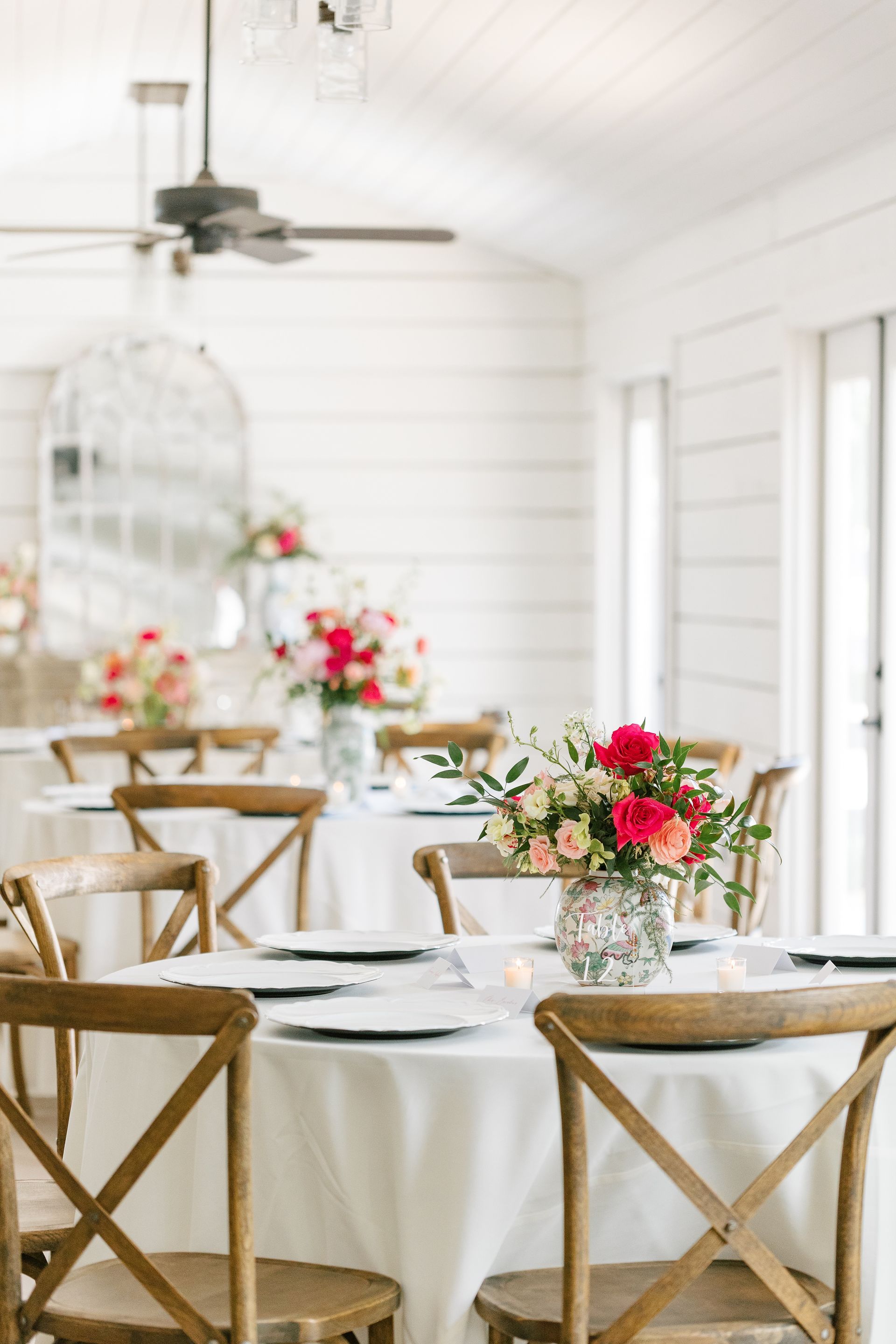 Elegant white dining room with wooden chairs and tables set with floral centerpieces