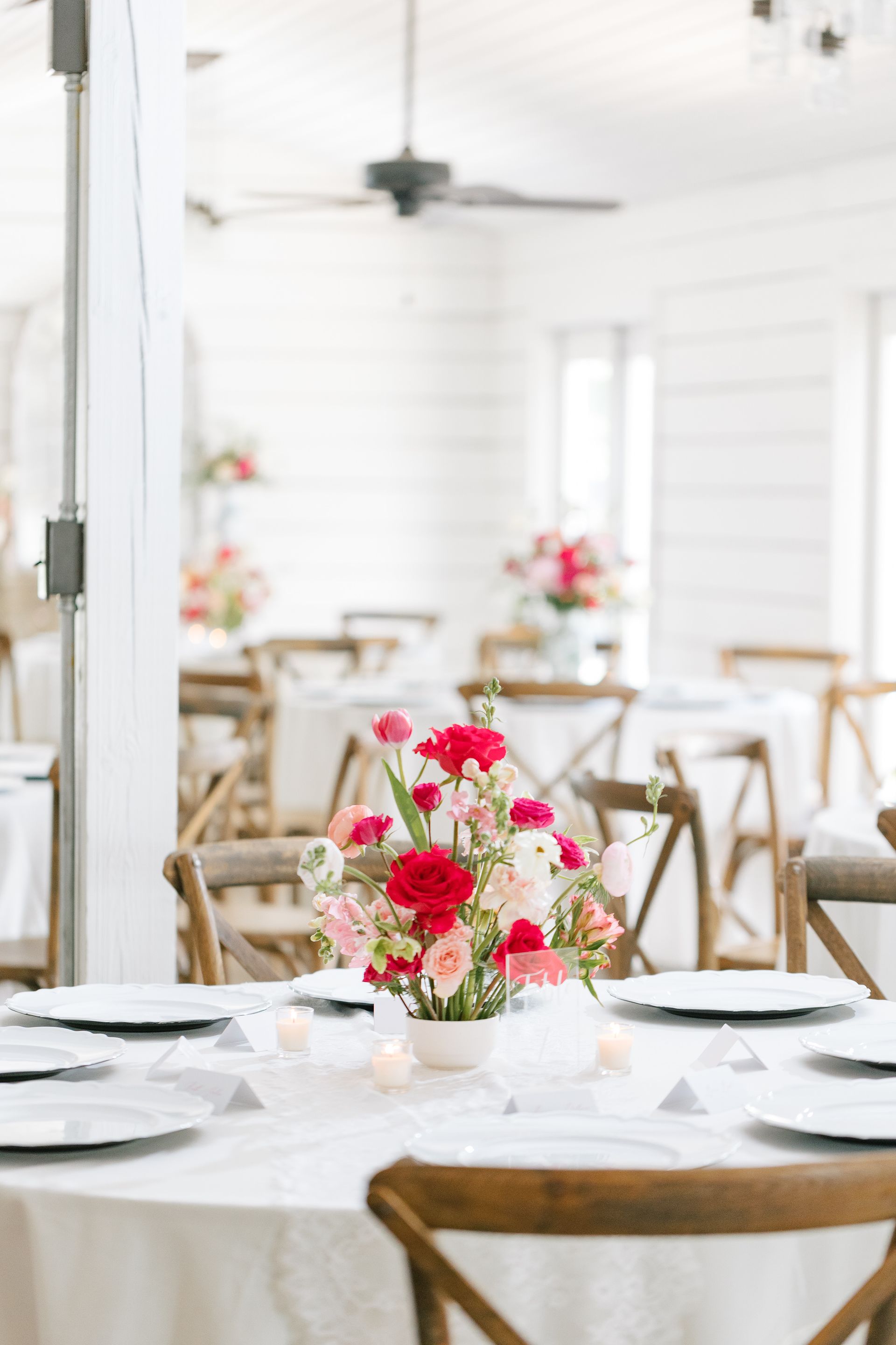White dining tables with floral centerpieces in a bright event venue