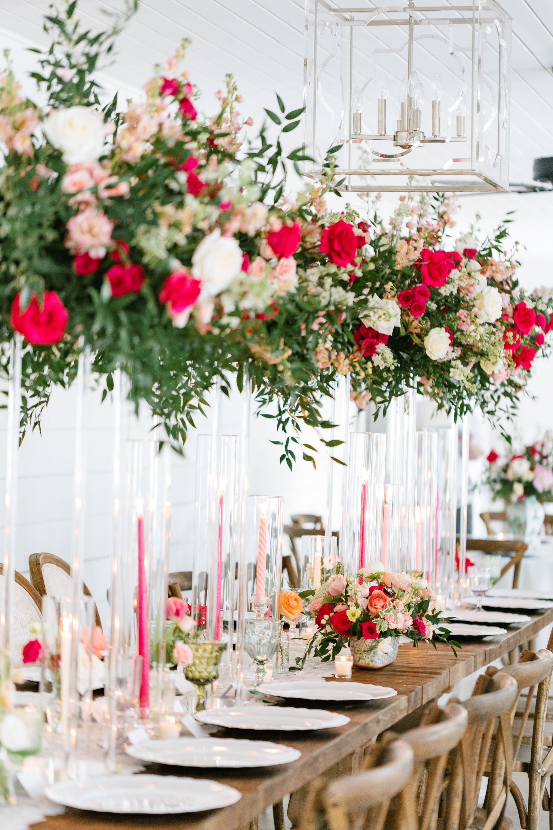 Elegant dining table beneath cascading pink, white, and red floral arrangements in a bright event venue