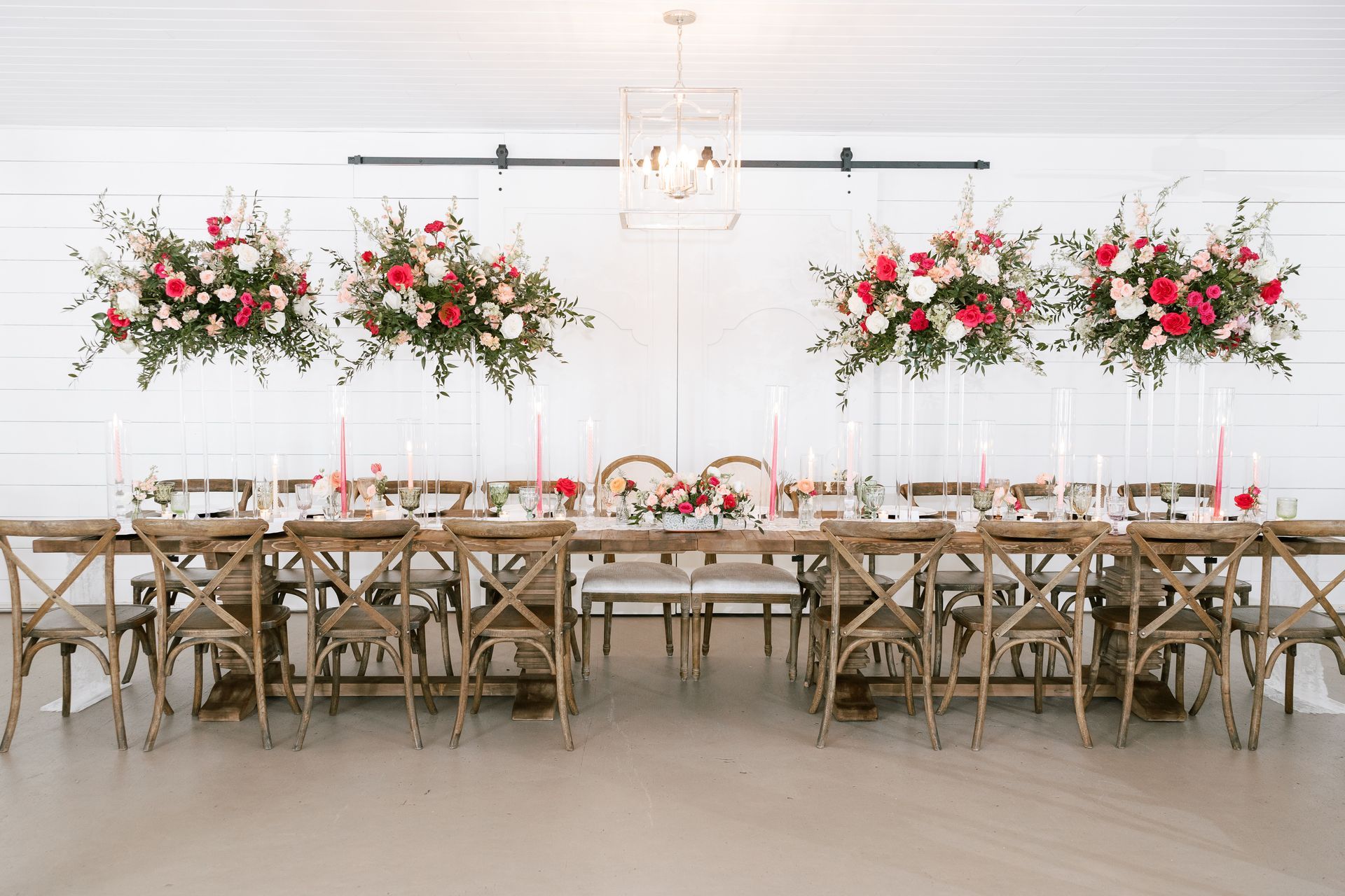 Elegant white banquet table with floral centerpieces and rustic wooden chairs in a bright room