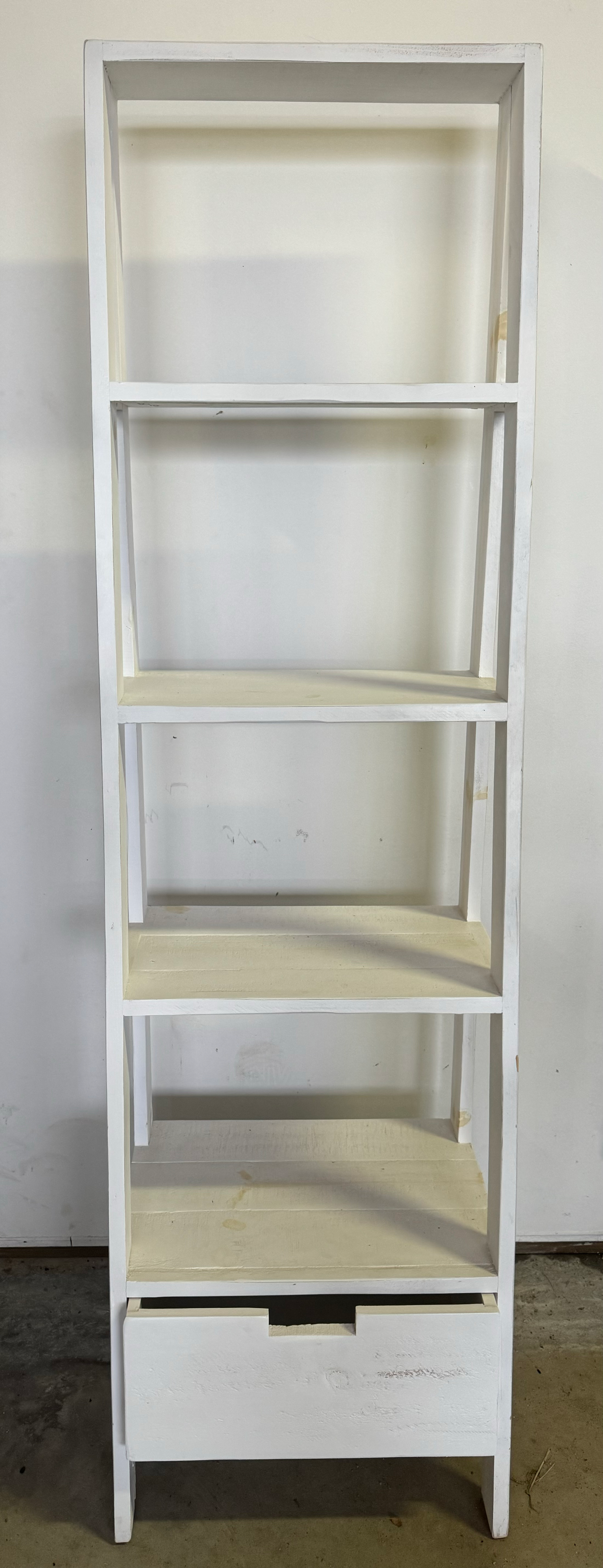 White five-shelf shelving unit with a drawer at the bottom, standing against a plain wall.