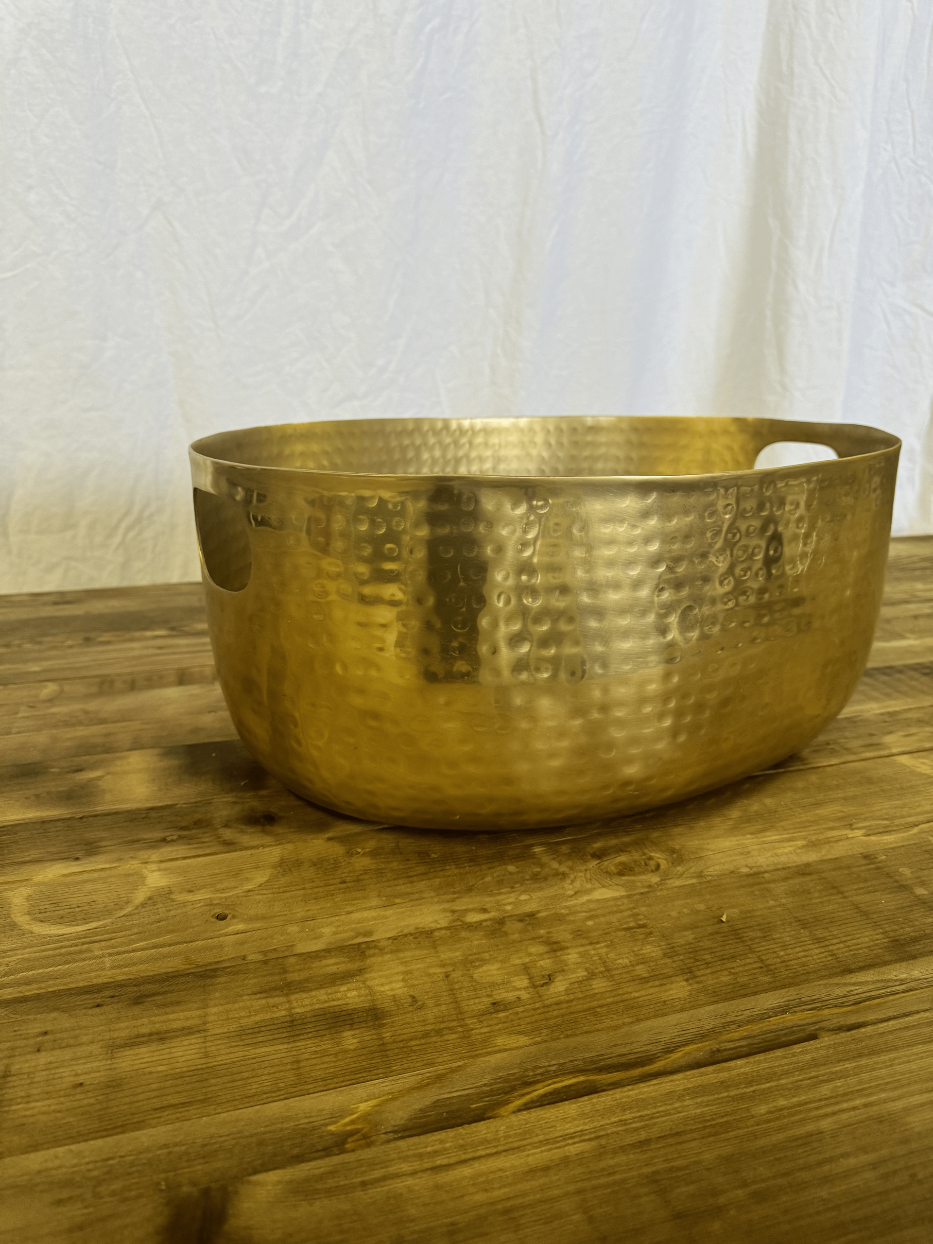Gold hammered metal bowl on a wooden surface against a light background