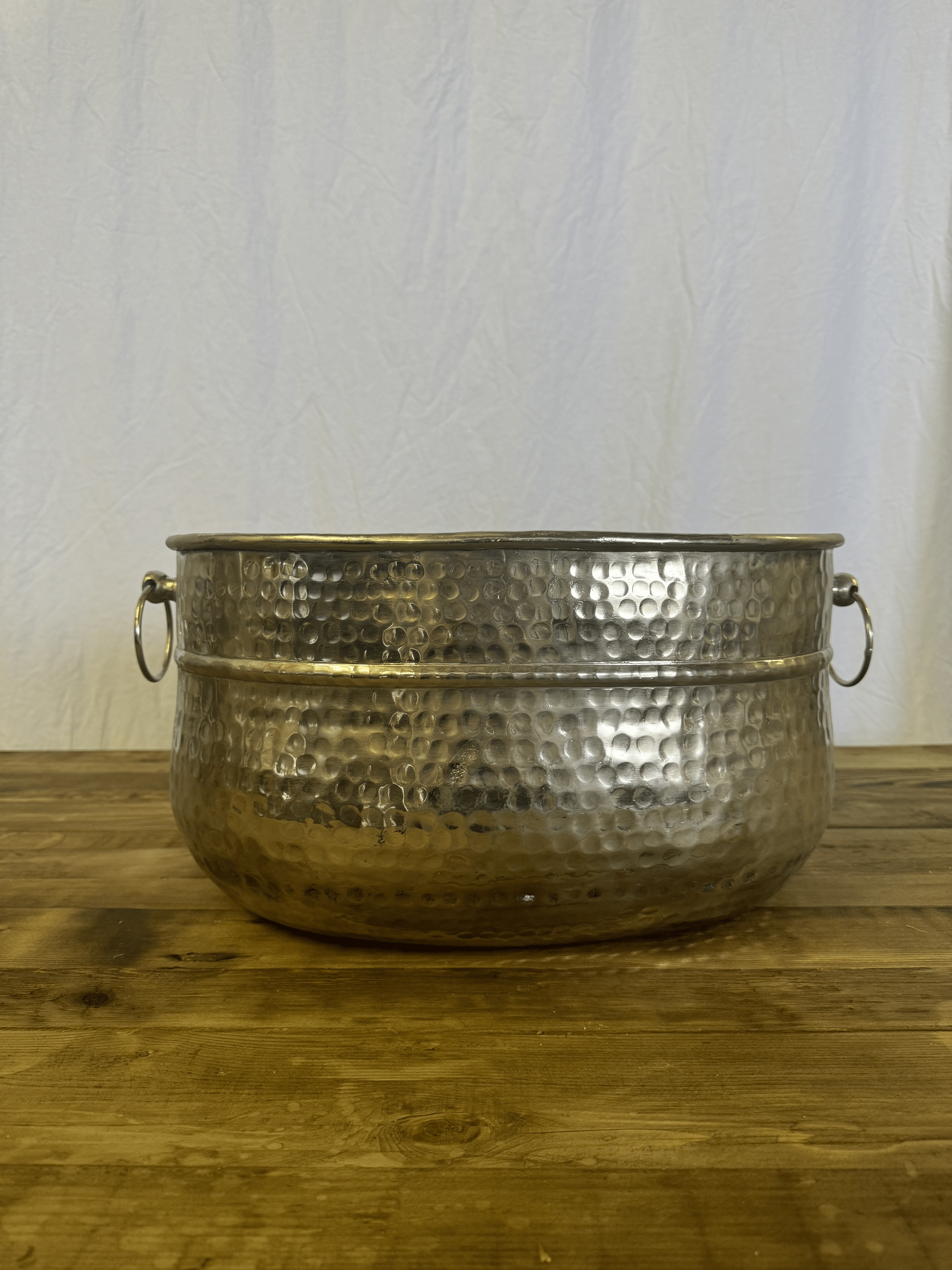 Hammered metal bowl with side handles on a wooden table against a light wall