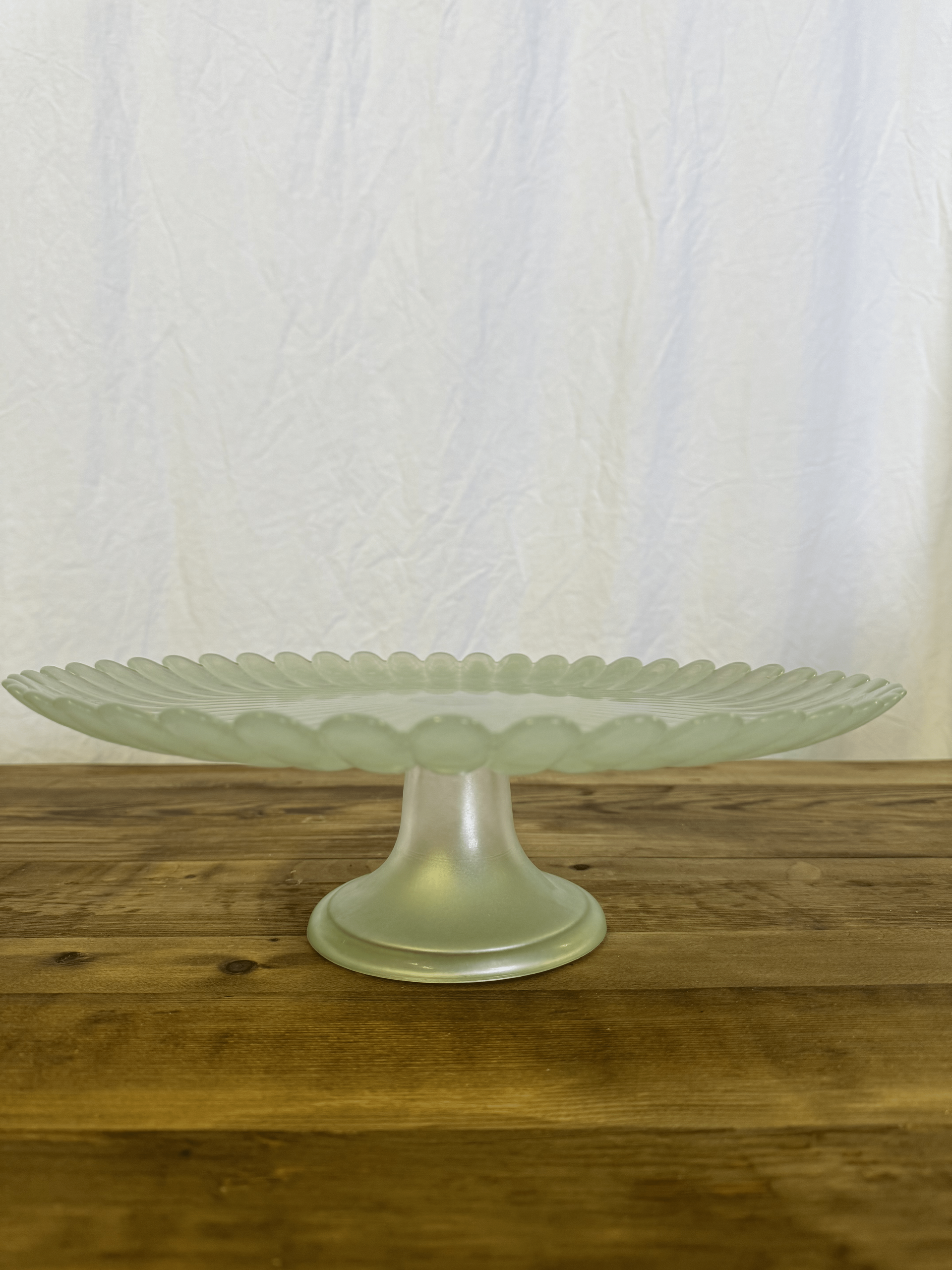 Clear glass pedestal serving dish on a wooden table against a white backdrop