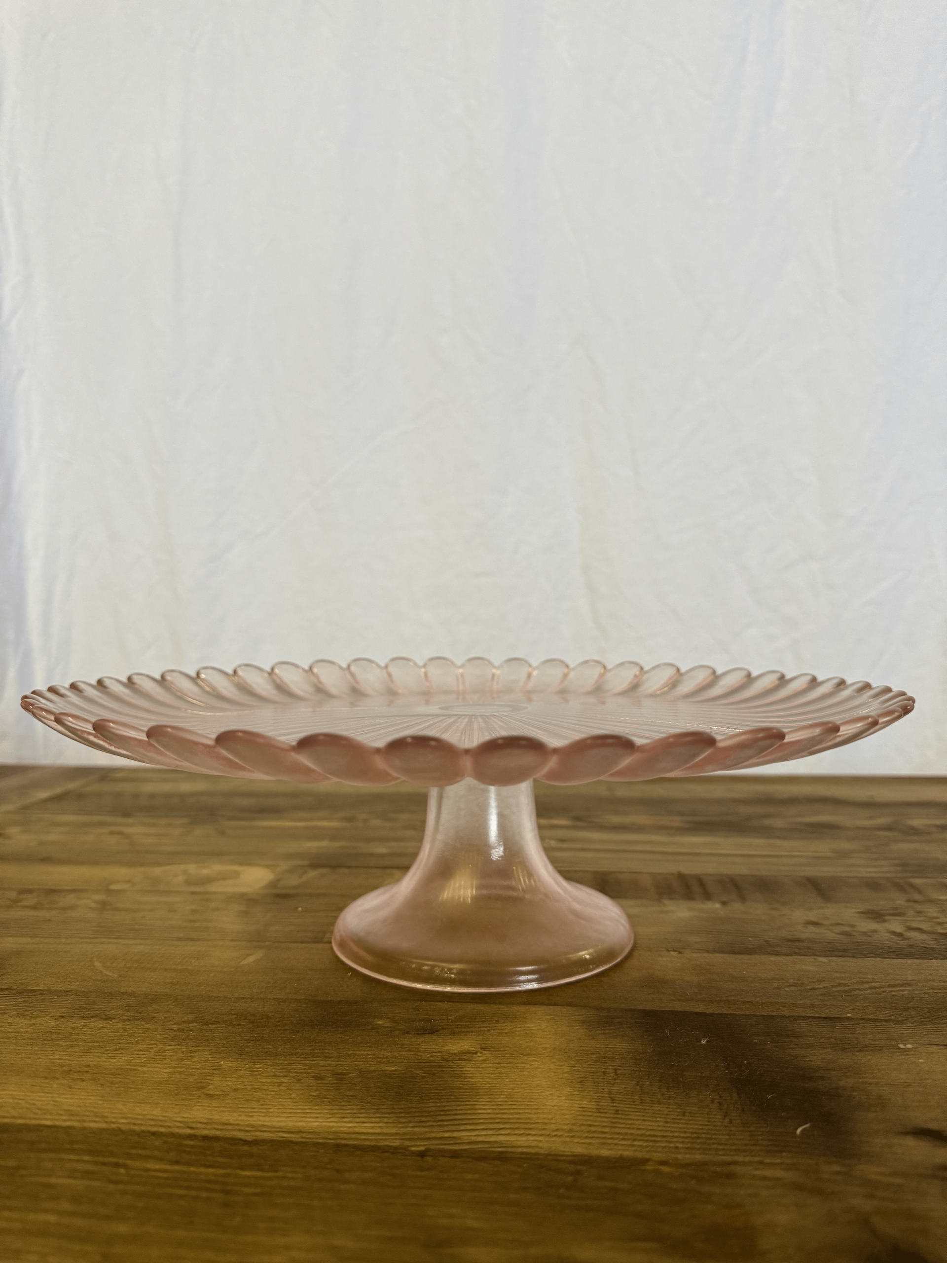 Pink glass pedestal cake stand on a wooden table against a plain white background