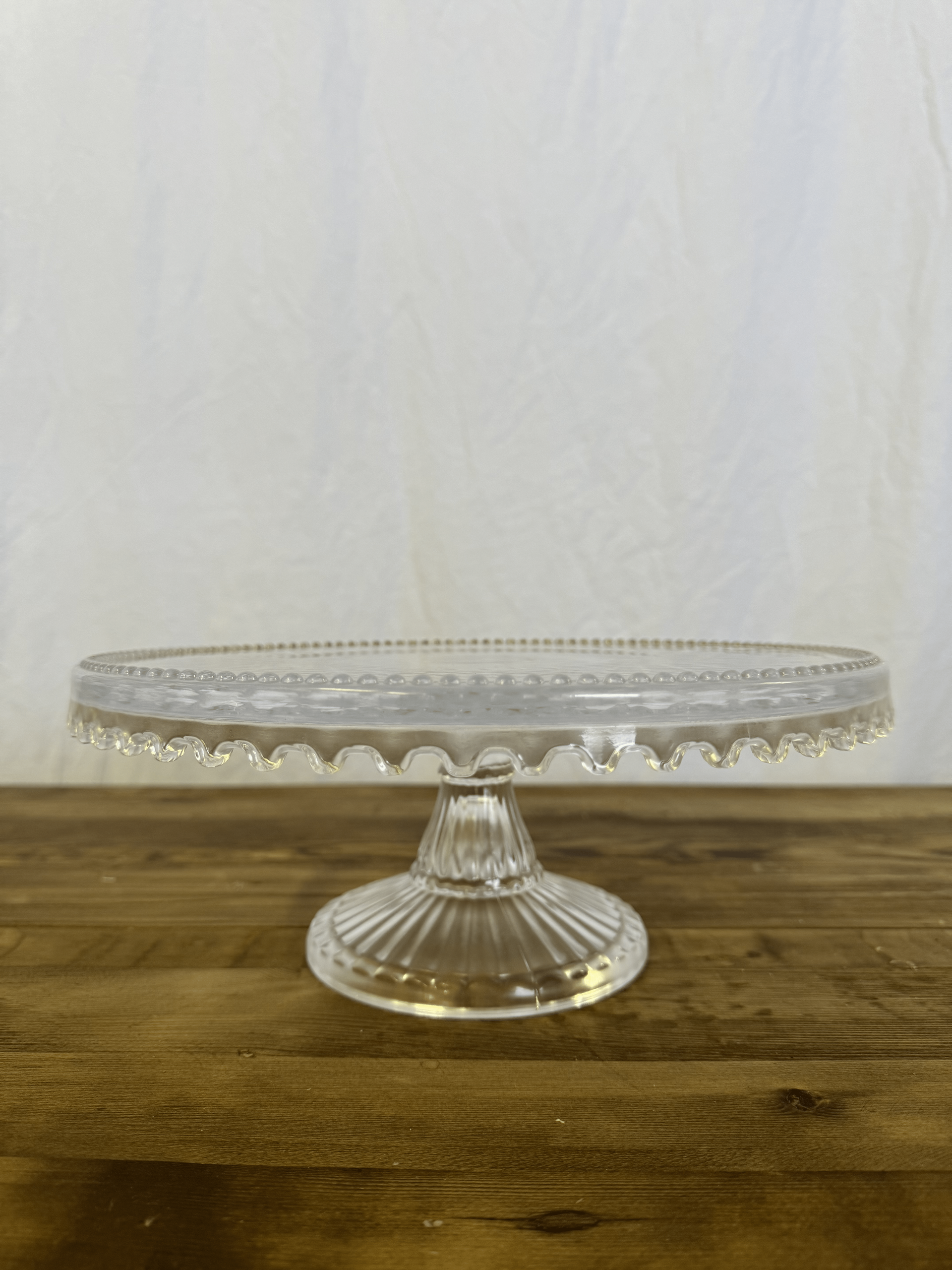 Clear glass cake stand on a wooden table against a plain light background
