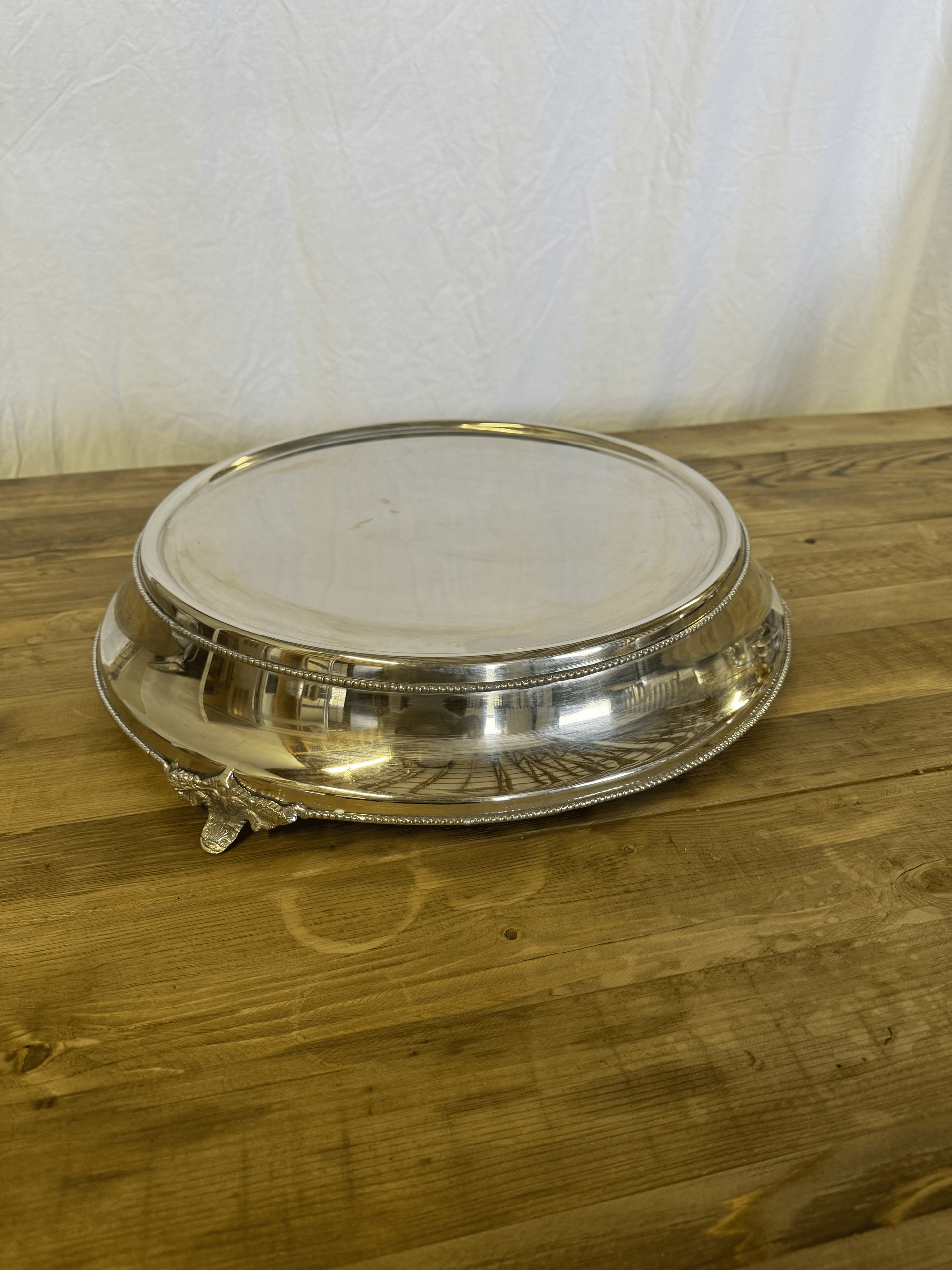 Silver serving tray with a white center resting on a wooden table against a light wall